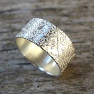 May include: A silver band ring with a fern leaf design. The ring is wide and has a textured surface.
