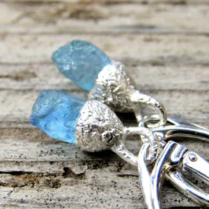 May include: A pair of silver earrings with blue crystal stones. The earrings have a textured silver setting and a hook closure.