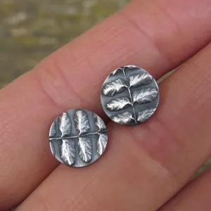 May include: A pair of silver earrings with a leaf design. The earrings are round and have a textured surface.