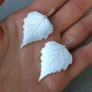 May include: A pair of silver earrings shaped like birch leaves. The leaves are detailed and have a textured surface.