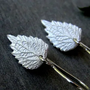 May include: A pair of silver earrings shaped like leaves. The leaves have a detailed, textured design.