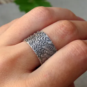 May include: A wide silver band ring with a textured design of leaves and branches.