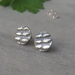 May include: A pair of silver stud earrings with a leaf design. The earrings are round and have a textured surface.