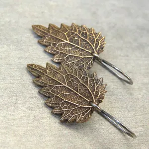 May include: A pair of bronze leaf earrings with silver hooks. The leaves are detailed with veins and have a natural, organic look.