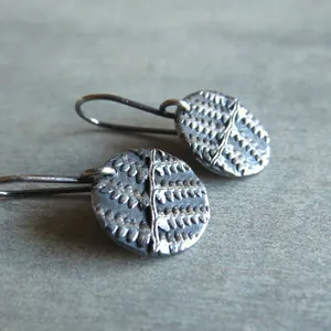 May include: A pair of silver earrings with a textured, geometric design. The earrings are made of metal and have a circular shape.