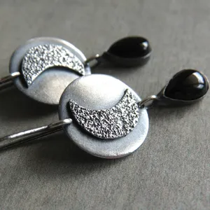 May include: A pair of silver earrings with a textured crescent moon design and black teardrop-shaped stones.