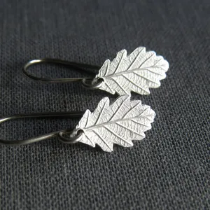 May include: A pair of silver earrings with a detailed oak leaf design. The leaves are textured and have a delicate, natural look.