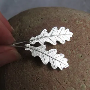 May include: Silver oak leaf earrings with a textured finish. The earrings are hanging from a silver hook.