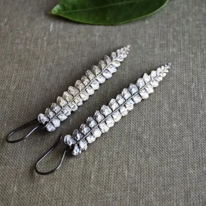 May include: A pair of silver fern earrings with black wire hooks. The earrings are made of metal and have a delicate, natural look.